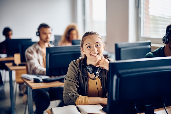 Happy female student using desktop PC during computer class and looking at camera.