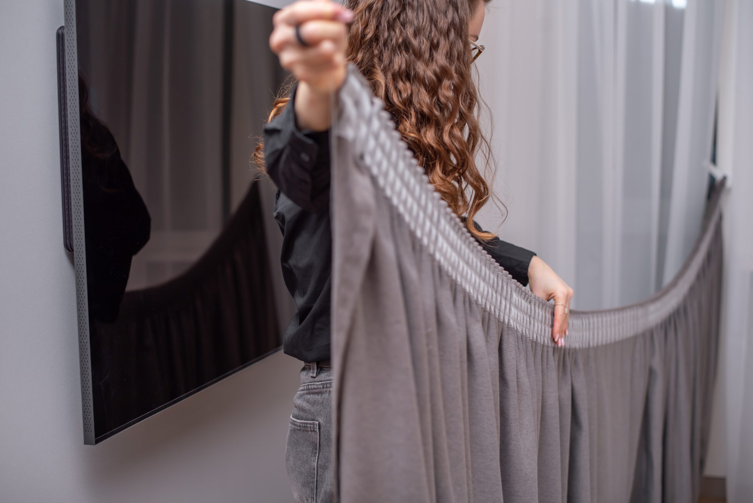 A female designer is making pleats on gray curtain to hang it on the window