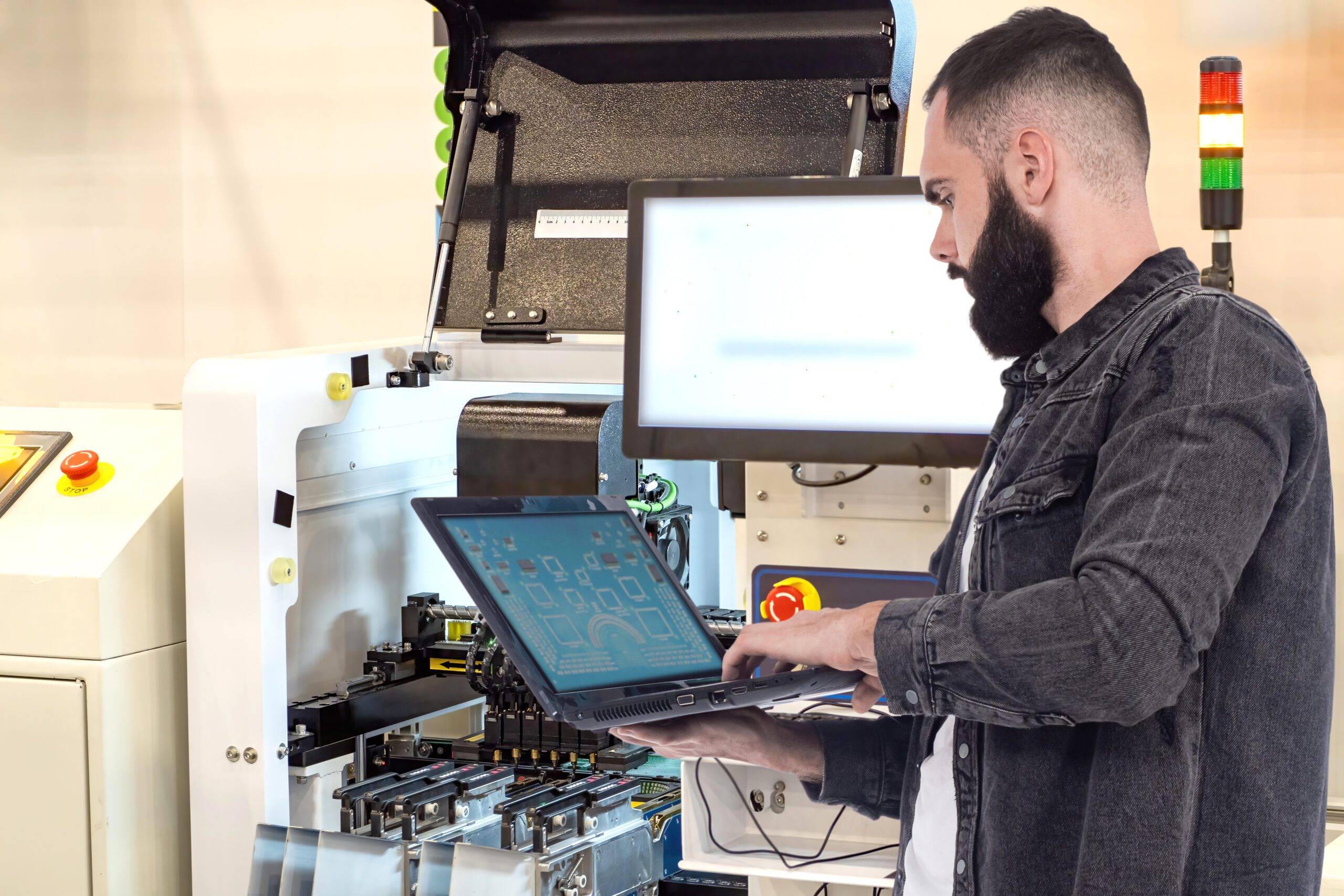 Technician programs and monitors automated manufacturing equipment using a laptop, working in the field of industrial automation and electronics production.