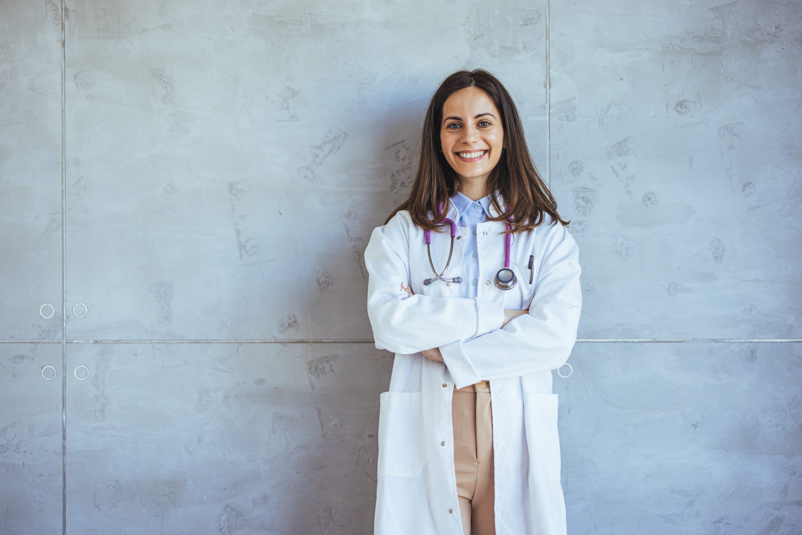 Confident Female Doctor Smiling Against Modern Gray Background in Medical Attire