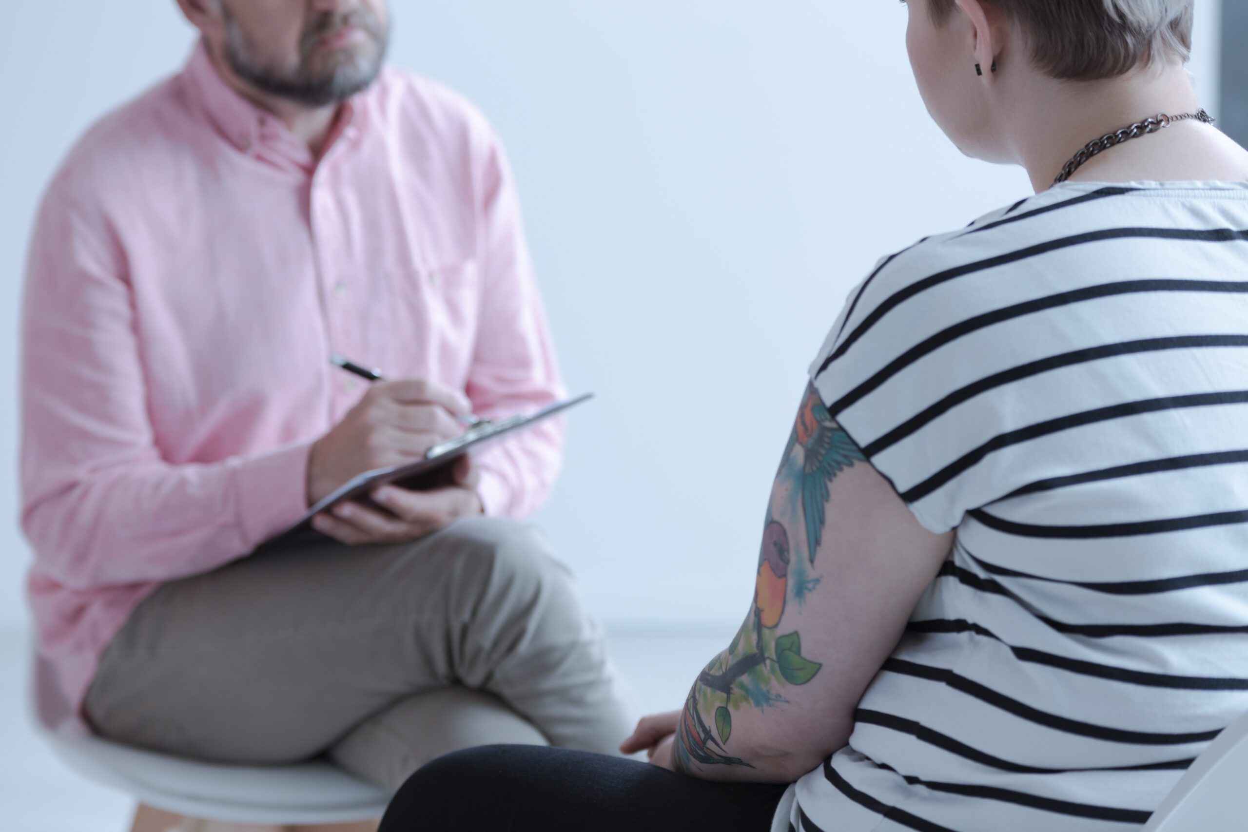 Close-up of a therapy specialist taking notes while listening to a tattooed young person with emotional and behavioral problems in a juvenile detention center.