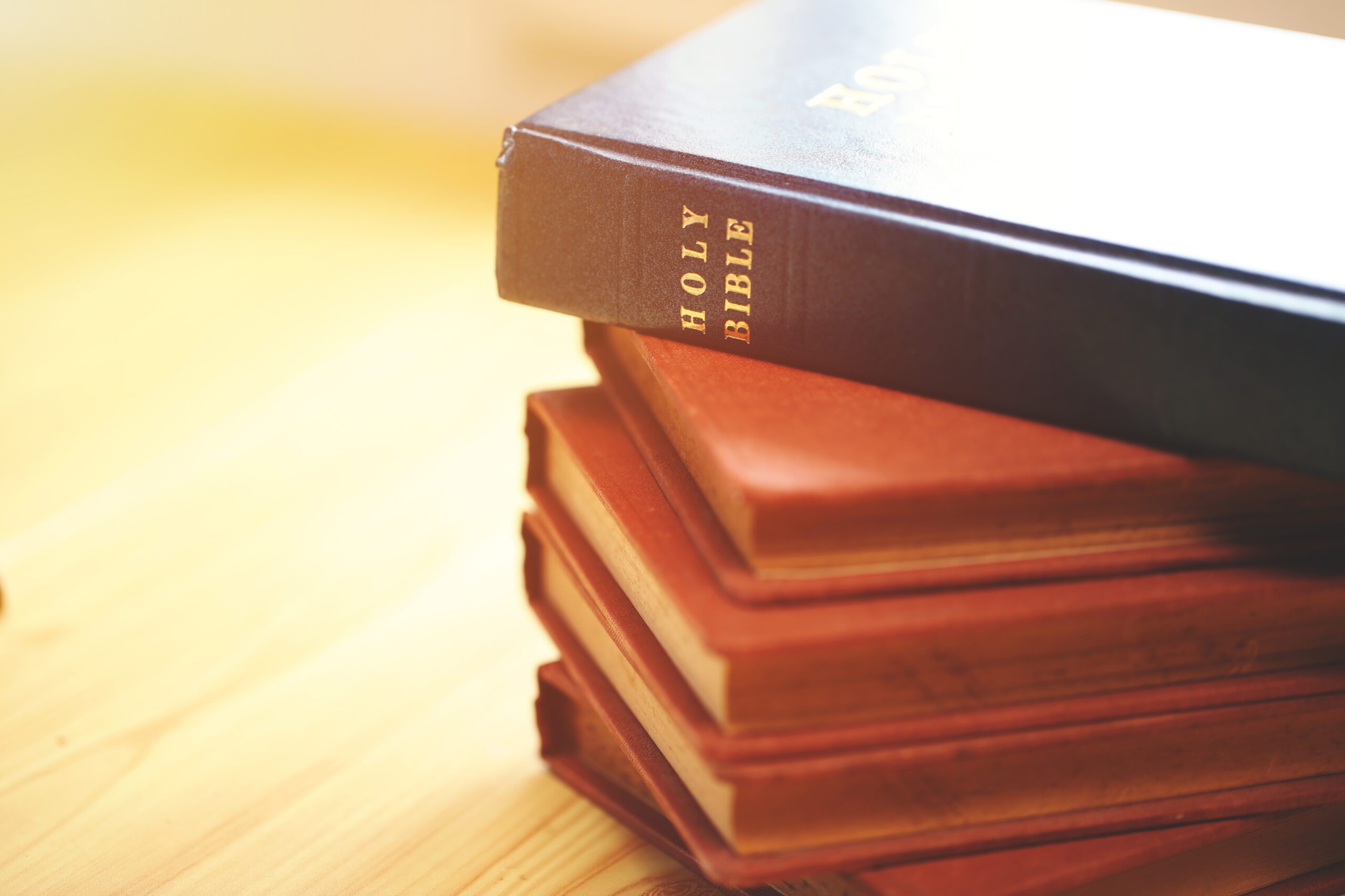 Stack of vintage Bibles with a close-up focus on the spine of a blue Holy Bible on top. Represents religious study, Christian faith, scripture preservation, and spiritual tradition.